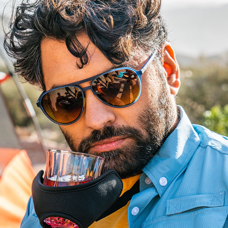 Een bebaarde man met een blauwe pilotenzonnebril snuift whisky uit een glazen houder die zo uit een Skymall-catalogus zou kunnen komen.