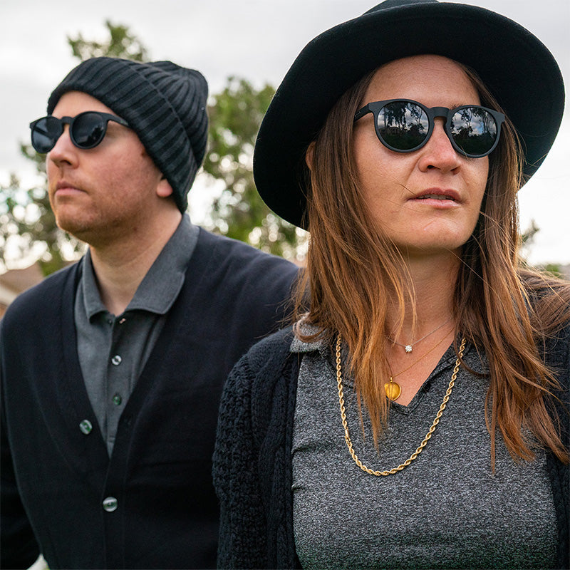Een hipster man en vrouw in chique zwarte outfits dragen een ronde zwarte zonnebril met niet-reflecterende zwarte glazen.