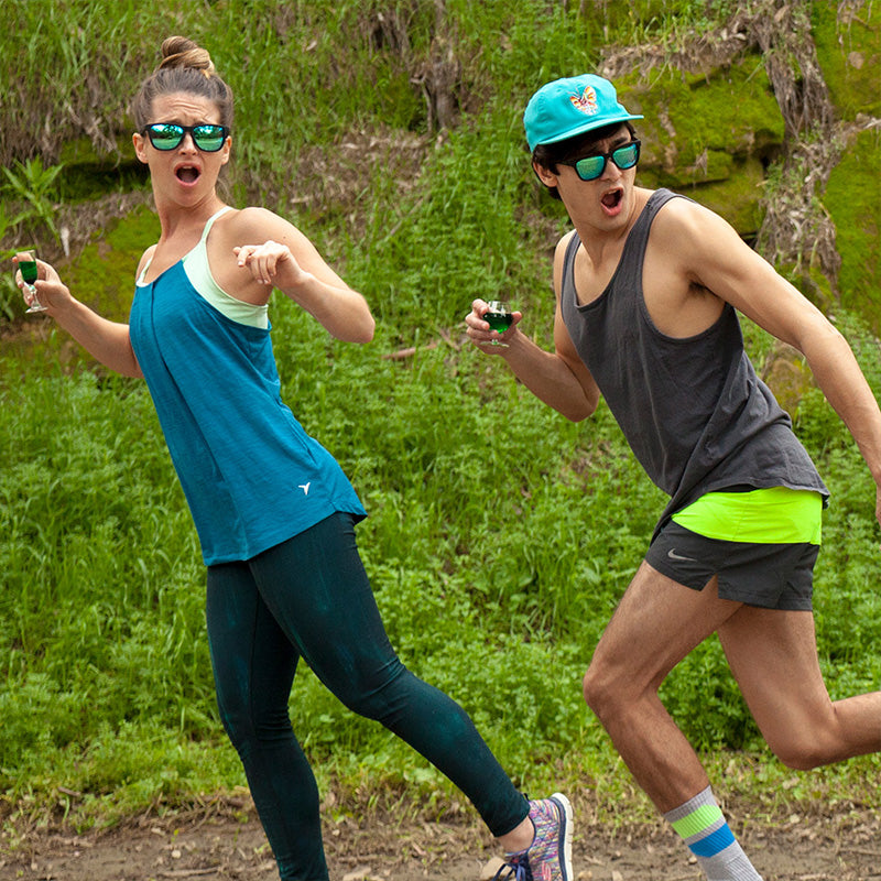 Twee hardlopers met een zwarte zonnebril met groene reflecterende glazen kijken bang over hun schouders terwijl ze in een weiland joggen.