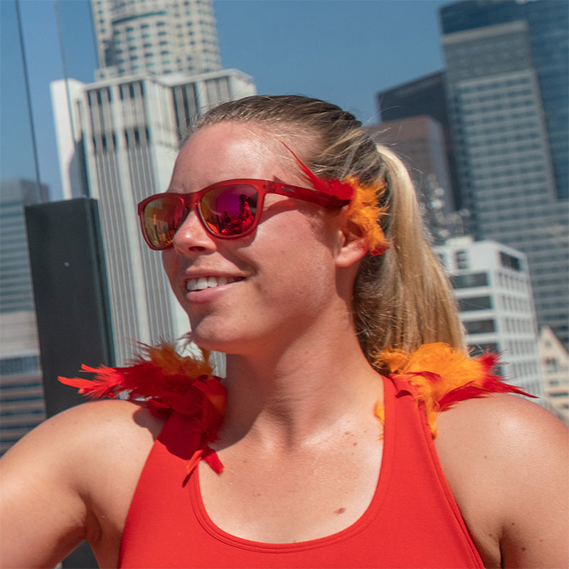 Een vrouw draagt een rode zonnebril met rode glazen met rode en oranje veeraccenten, een skyline van een stad achter haar.