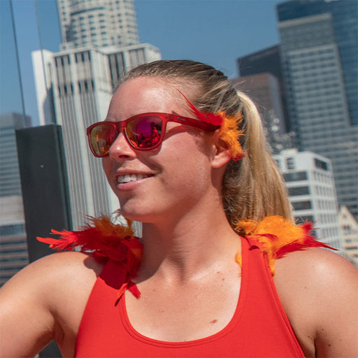 Een vrouw draagt een rode zonnebril met rode glazen met rode en oranje veeraccenten, een skyline van een stad achter haar.